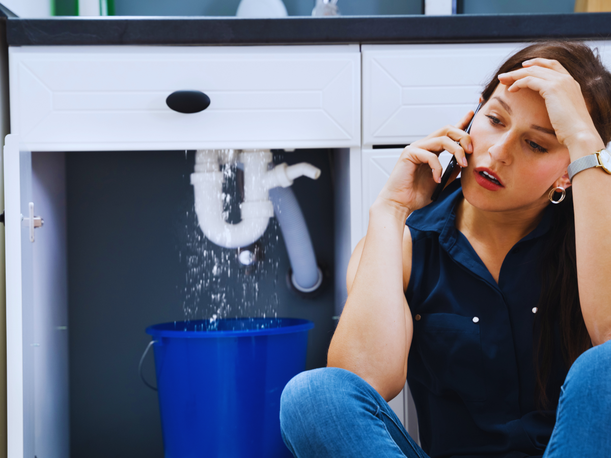 Homeowner calling plumber because of plumbing leak under sink